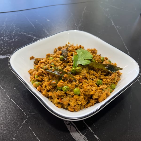 A white square bowl filled with a savory brown and green pea dish, garnished with cilantro.