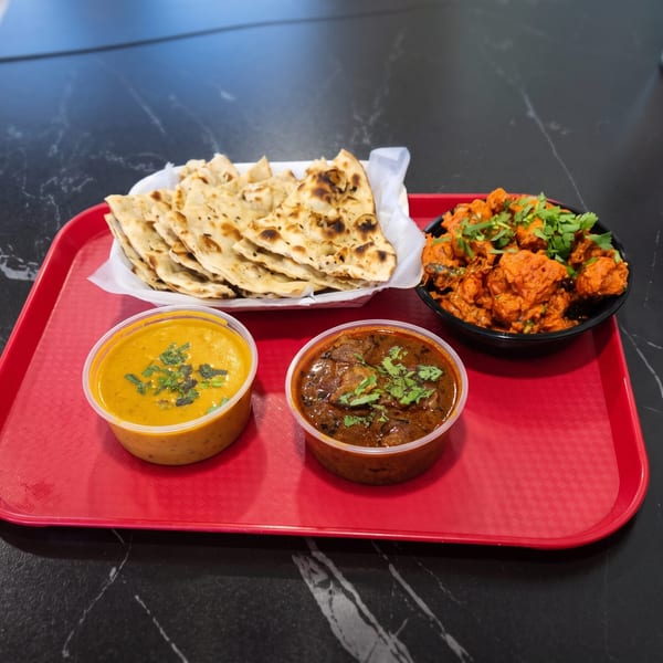 Indian meal on a red tray with naan, chicken tikka, and two curries on a black marble table.