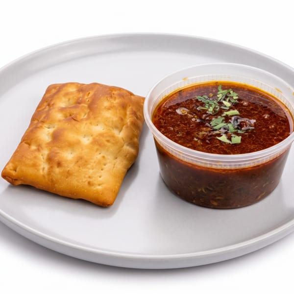 A golden-brown flatbread and a clear container of chili with green herbs on a white plate.